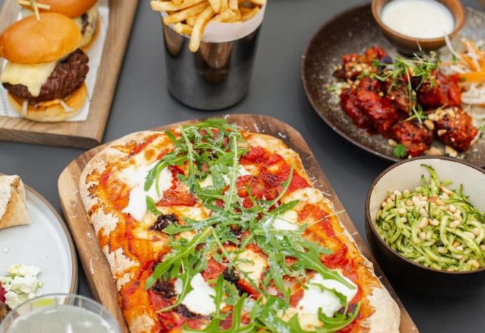 Native Manchester gay-friendly hotel food. Pizza, fries, sliders, wings, and salad on a table. Delicious dining at a Manchester hotel.