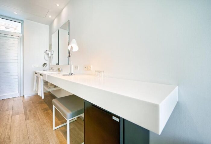 Hotel Nayra Adults Only gay-friendly hotel bathroom. Minimalist design with white counter, stool, and wood-look tile floor. Modern, clean aesthetic.