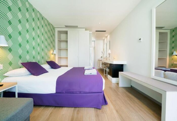Hotel Nayra Adults Only gay-friendly room. Modern bedroom with green patterned wallpaper, purple accents, and sleek white furniture.
