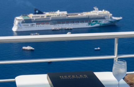 Gay-Friendly Hotel Nefeles Luxury Suites view. Cruise ship, drink, and menu on a table. Gay travel in Santorini, Greece.