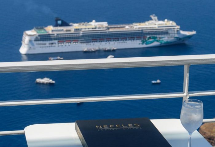 Gay-Friendly Hotel Nefeles Luxury Suites view. Cruise ship, drink, and menu on a table. Gay travel in Santorini, Greece.