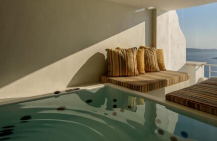 Nefeles Luxury Suites gay-friendly hotel: Jacuzzi and striped cushions on a sunlit terrace overlooking the sea in Santorini, Greece.