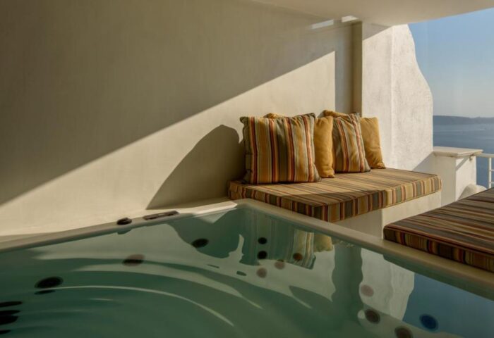 Nefeles Luxury Suites gay-friendly hotel: Jacuzzi and striped cushions on a sunlit terrace overlooking the sea in Santorini, Greece.