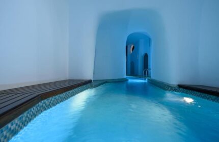 Nefeles Luxury Suites gay-friendly hotel pool. Indoor pool with blue lighting, white walls, and wood accents. Ideal for gay travel.