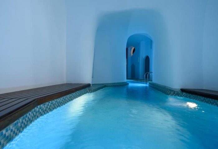 Nefeles Luxury Suites gay-friendly hotel pool. Indoor pool with blue lighting, white walls, and wood accents. Ideal for gay travel.