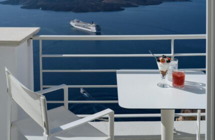 Nefeles Luxury Suites gay-friendly hotel balcony view. Cruise ship on the sea. Dessert and drink on table. Gay travel advice.