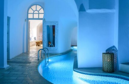 Nefeles Luxury Suites' gay-friendly hotel. Indoor pool with blue lighting, white walls, and arched doorways. Ideal gay travel destination.
