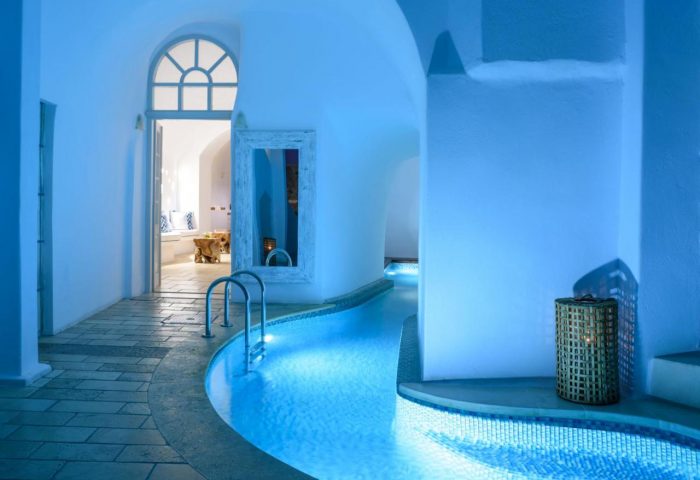 Nefeles Luxury Suites' gay-friendly hotel. Indoor pool with blue lighting, white walls, and arched doorways. Ideal gay travel destination.
