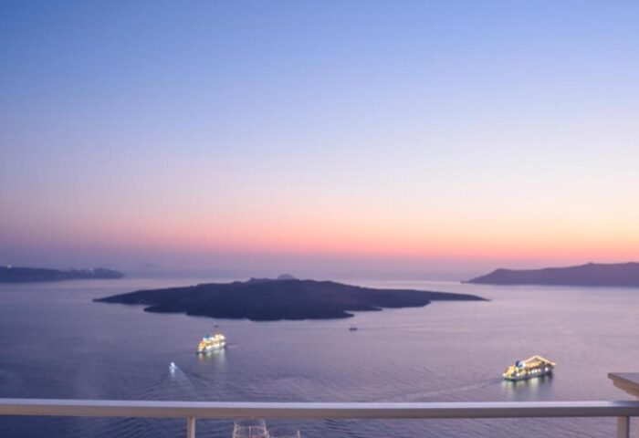Sunset view from Nefeles Luxury Suites, a gay-friendly hotel. Wine glasses on table, sea view. Perfect for gay travel in Santorini.