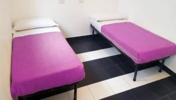 New Generation Hostel Milan Center: Gay-friendly hotel room with two single beds and purple blankets, black and white striped floor.