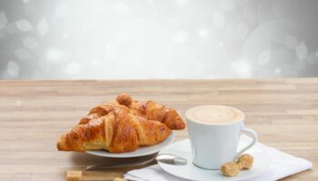 New Generation Hostel Milan Center: Croissants and coffee cup on a wooden table. Breakfast at a gay-friendly hotel in Milan.