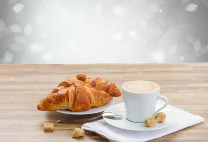 New Generation Hostel Milan Center: Croissants and coffee cup on a wooden table. Breakfast at a gay-friendly hotel in Milan.