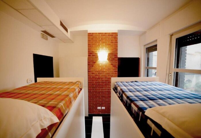 New Generation Hostel Milan Center gay-friendly room. Bunk beds with colorful plaid bedding, brick wall, and modern design. Perfect for gay travelers.