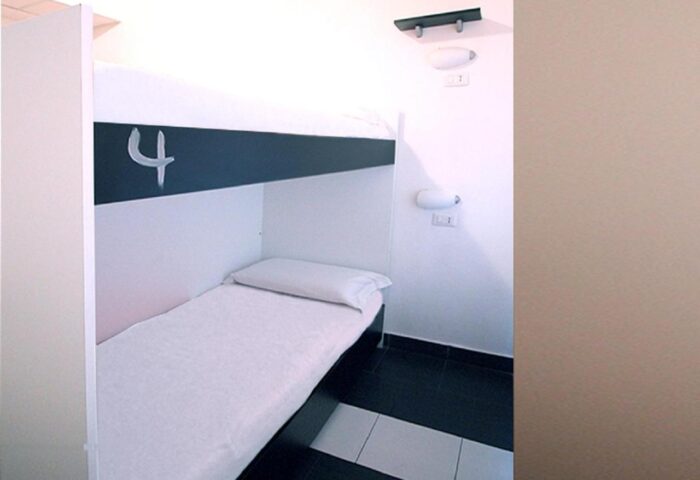 New Generation Hostel Milan Center gay-friendly room. Bunk bed with white sheets and pillow. Black and white floor tiles. Room number 4.
