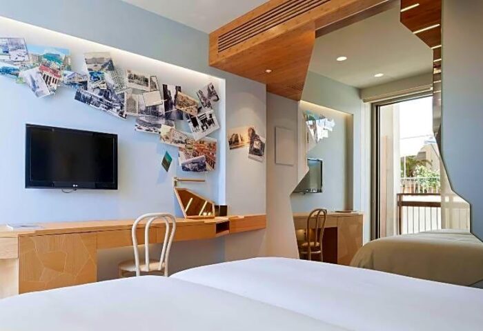 Gay-friendly New Hotel room. Modern interior with TV, desk, pictures on the wall, and a balcony view. Ideal for gay men's travel.