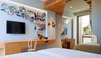Gay-friendly New Hotel room. Modern interior with TV, desk, pictures on the wall, and a balcony view. Ideal for gay men's travel.