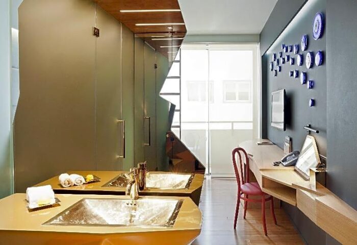 Gay-friendly New Hotel room: Modern bathroom with double sinks, desk, chair, and TV. Stylish design for gay men's travel.