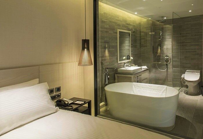 New Riverview Suites gay-friendly hotel room. Features a bed, bedside table, and a bathroom with a tub, sink, mirror, shower, and toilet.