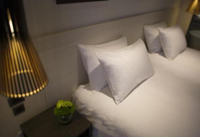 New Riverview Suites gay-friendly hotel room. Crisp white linens, plush pillows. Modern lamp and bedside table. A comfortable stay for gay travelers.
