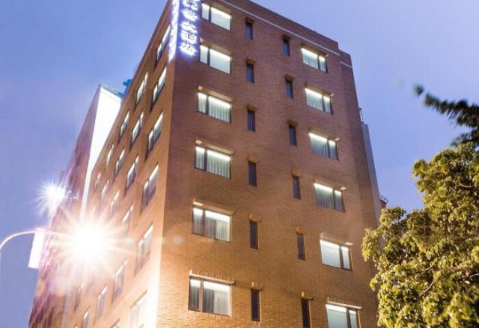 Exterior of New Riverview Suites, a gay-friendly hotel. The building is tall and made of brick, with many windows. Nighttime view.