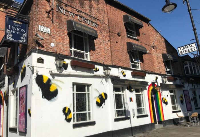 New Union Guesthouse, a gay-friendly hotel on Canal Street. The building features bee artwork and a rainbow flag, symbolizing LGBTQ+ pride.