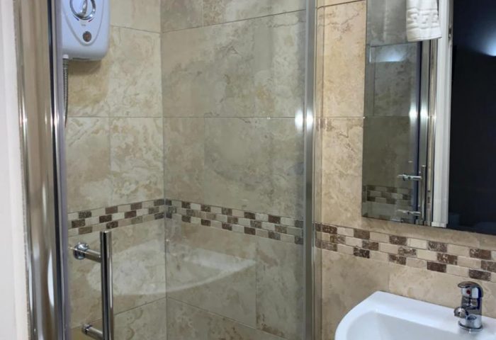 Bathroom at New Union Guesthouse, a gay-friendly hotel. Shower stall with glass door, sink, mirror, and tiled walls. Ideal for gay travelers.
