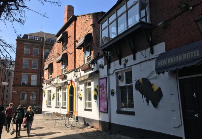 New Union Guesthouse, a gay-friendly hotel. Exterior view with bee art, rainbow door, and people walking by. Manchester travel advice.