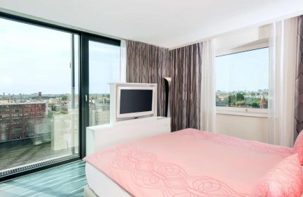 Nhow Berlin Hotel room with a view. Gay-friendly hotel featuring a pink bed, TV, and large window overlooking the city. Modern design.