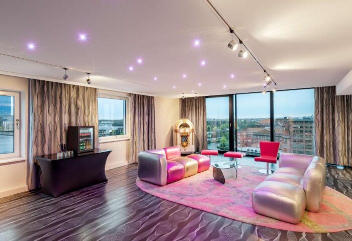 Nhow Berlin Hotel room with pink rug, jukebox, sofas, and city view. Gay-friendly hotel design, vibrant and modern. Berlin travel advice.