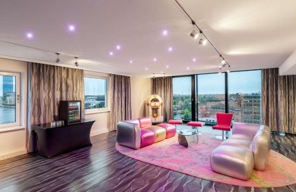 Nhow Berlin Hotel room with pink rug, jukebox, sofas, and city view. Gay-friendly hotel design, vibrant and modern. Berlin travel advice.