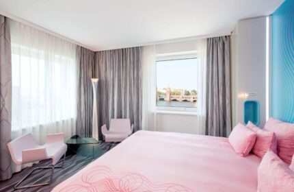 Nhow Berlin Hotel room. Gay-friendly hotel with pink bed, chairs, and view of the Oberbaum Bridge. Modern design, perfect for gay travel.