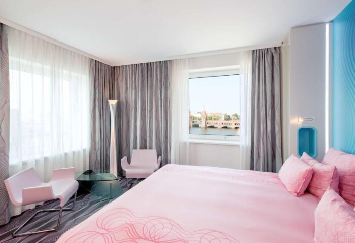Nhow Berlin Hotel room. Gay-friendly hotel with pink bed, chairs, and view of the Oberbaum Bridge. Modern design, perfect for gay travel.