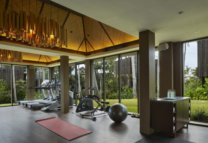 Nirjhara Bali gay-friendly hotel gym. Treadmills, exercise bike, yoga mat, and fitness ball. Tropical greenery visible through large windows.
