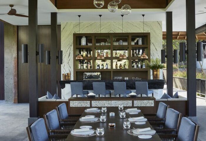 Dining area at Nirjhara Bali, a gay-friendly hotel. Long table set for dinner, bar in background. Luxury travel for gay men in Bali.