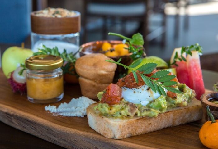 Gourmet breakfast at Nirjhara Bali, a gay-friendly hotel. Toast with avocado, poached egg, fruit, and pastries on a wooden board. Delicious!