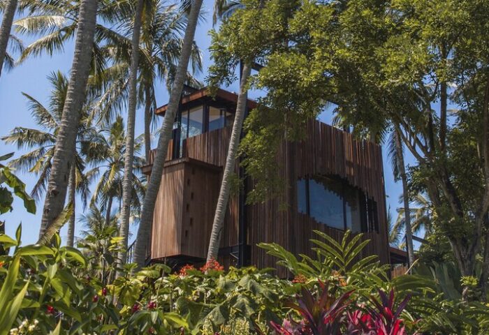 Nirjhara Bali gay-friendly hotel room. Wooden structure with large window surrounded by palm trees and lush tropical vegetation. Bali travel.