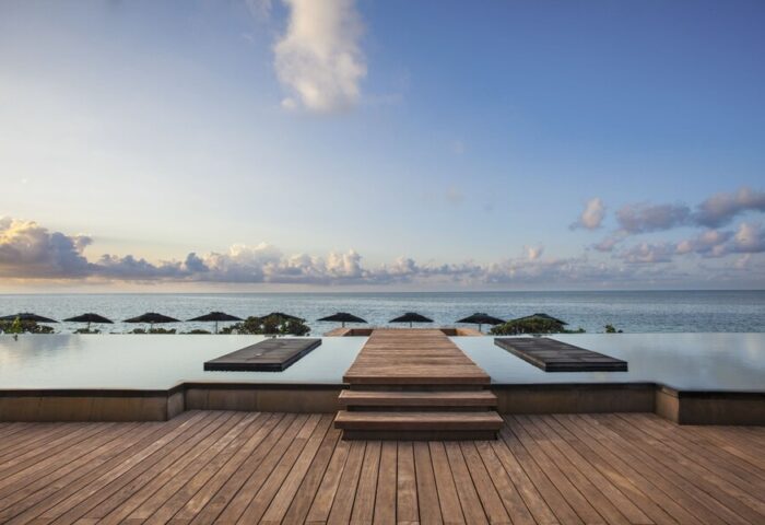 Nizuc Resort & Spa infinity pool view. Gay-friendly hotel in Cancun, Mexico. Ocean view, wooden deck, and sun umbrellas. Relaxing travel destination.