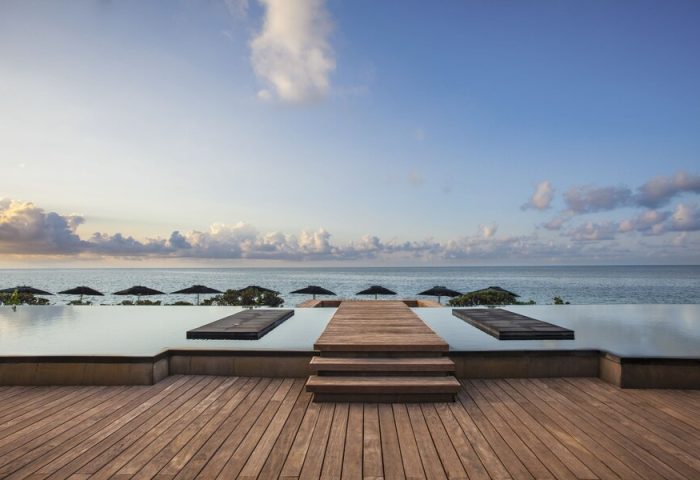Nizuc Resort & Spa infinity pool view. Gay-friendly hotel in Cancun, Mexico. Ocean view, wooden deck, and sun umbrellas. Relaxing travel destination.