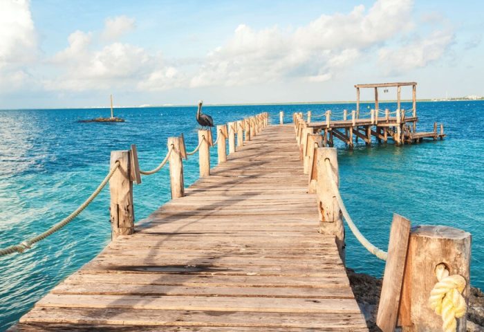 Wooden pier at Nizuc Resort and Spa, a gay-friendly hotel. A pelican sits on a post, overlooking the turquoise water. Perfect for gay travel.