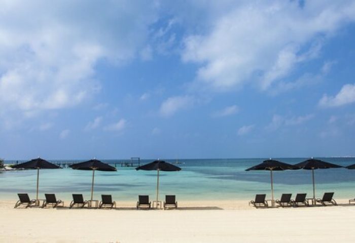 Beach view at Nizuc Resort and Spa, a gay-friendly hotel. Umbrellas and chairs line the sandy shore under a blue sky. Ideal gay travel spot.