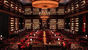 NoMad Las Vegas gay-friendly hotel library restaurant. Elegant dining room with bookshelves, red seating, and chandeliers. Upscale travel.