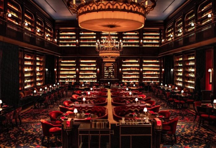 NoMad Las Vegas gay-friendly hotel library restaurant. Elegant dining room with bookshelves, red seating, and chandeliers. Upscale travel.