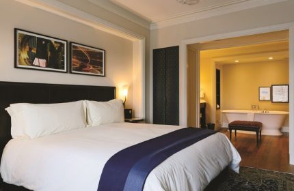 NoMad Las Vegas gay-friendly hotel room: King bed with white linens, dark headboard, and a view into the bathroom with a freestanding tub.