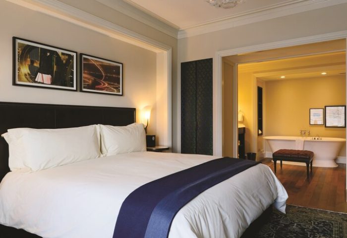 NoMad Las Vegas gay-friendly hotel room: King bed with white linens, dark headboard, and a view into the bathroom with a freestanding tub.