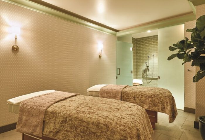 NoMad Las Vegas gay-friendly hotel spa. Two massage beds with brown covers, a shower room with green tiles, and a potted plant. Relaxing!