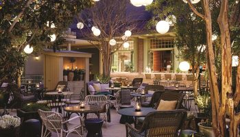 Gay-Friendly NoMad Las Vegas hotel outdoor patio. Tables and chairs under trees with globe lights. A perfect spot for gay travelers.