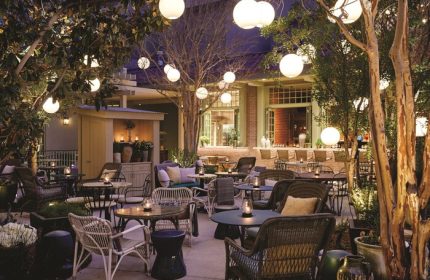 Gay-Friendly NoMad Las Vegas hotel outdoor patio. Tables and chairs under trees with globe lights. A perfect spot for gay travelers.