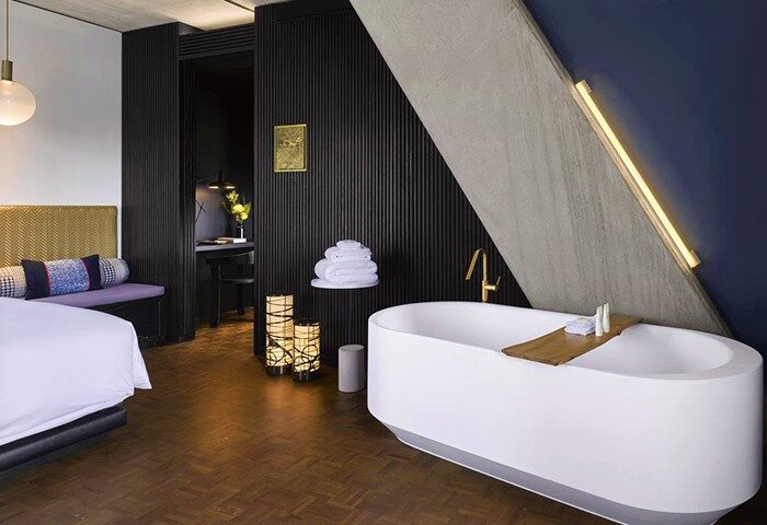 Nobu Hotel Shoreditch gay-friendly suite. Modern bathroom with white tub, wooden tray, and gold fixtures. Pet-friendly hotel room interior.