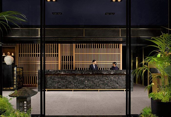 Nobu Hotel Shoreditch reception area. Gay-friendly, pet-friendly hotel with modern design. Staff at the desk, plants, and stone accents.