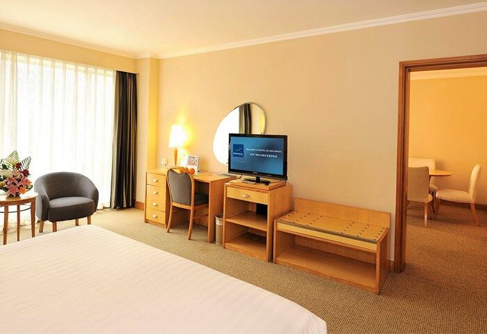 Novotel Beijing Xinqiao gay-friendly hotel room. Features a bed, desk, TV, seating area, and a view into an adjacent room with a dining table.